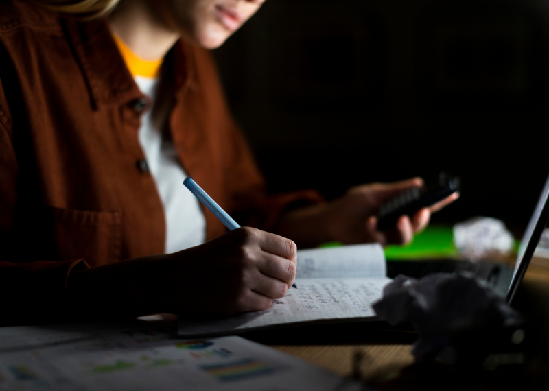 A focused virtual research assistant jotting down notes in a notebook while doing an competitor research.