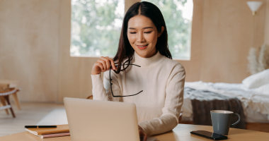 A virtual assistant looking at her laptop while holding her pair of spectacles in her hands.